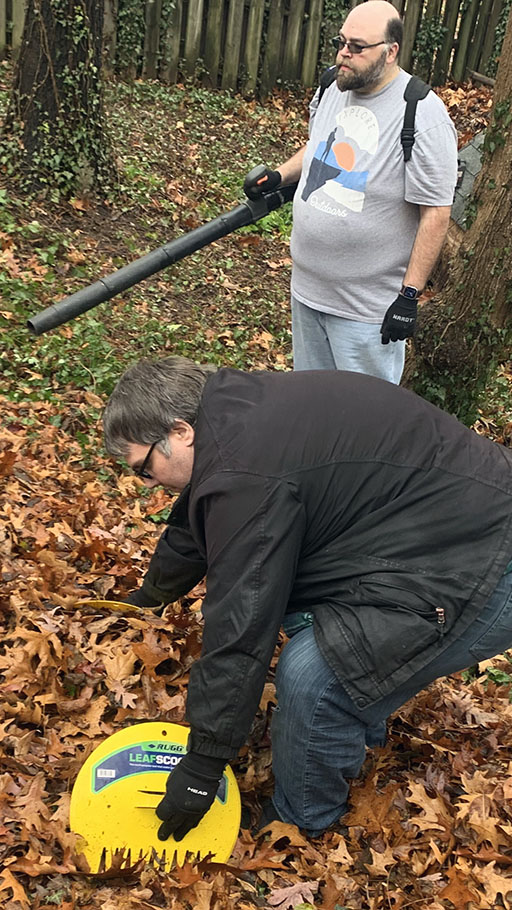 Mike Singleton operating a leaf blower while Lewie Moten gathers leaves.
