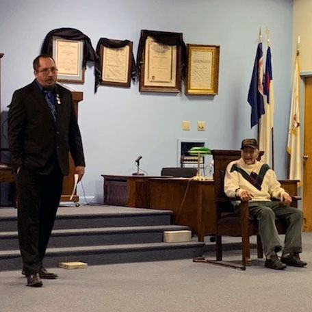 Worshipful Will Bryan stands beside Bill Woods chair giving a speech about Bills accomplishments on December 15, 2021